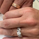 A 14k rose gold Barn Board wedding band displayed on a man’s hand with an 18k rose and white 1ct Enchanted Garden Engagement Ring on a woman’s hand.