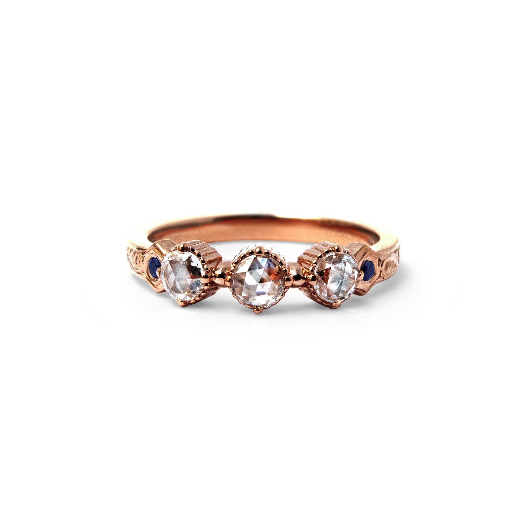 Crafted in 14KT rose gold, this ring features 3 round brilliant-cut diamonds in a row, with a blue sapphire on either side on a vintage-inspired hand engraved band.