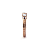 Crafted in 14KT rose gold, this ring features 3 round brilliant-cut diamonds in a row, with a blue sapphire on either side on a vintage-inspired hand engraved band.