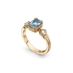 Crafted in 14KT yellow gold, this ring features an aquamarine between two round brilliant-cut diamonds on a vintage-inspired hand engraved band.