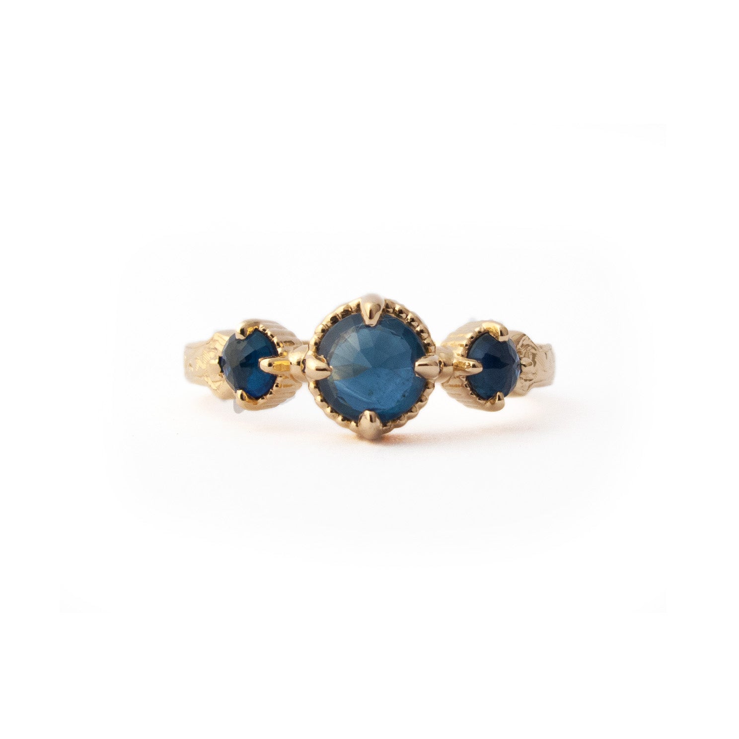 Crafted in 14KT yellow gold, this ring features a blue sapphire set between two smaller ones on a vintage-inspired hand engraved band.