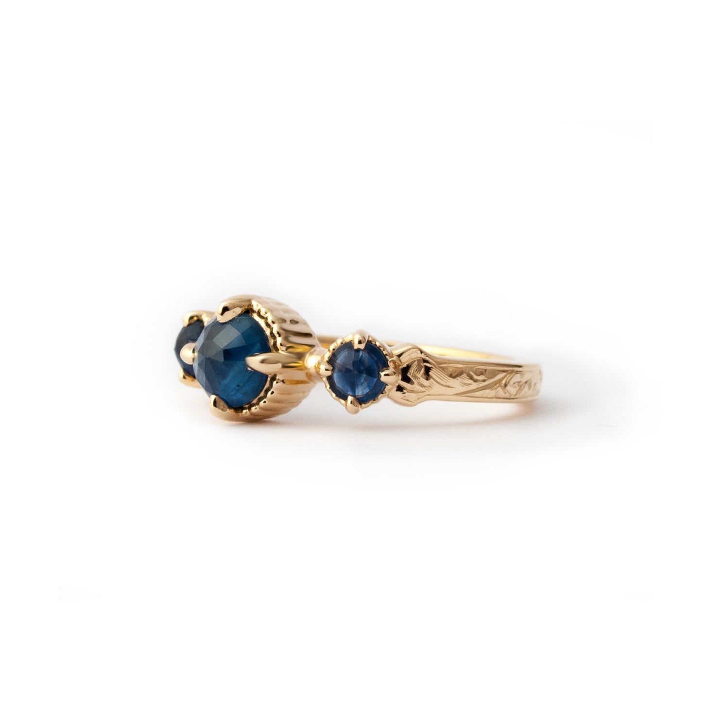 Crafted in 14KT yellow gold, this ring features a blue sapphire set between two smaller ones on a vintage-inspired hand engraved band. 