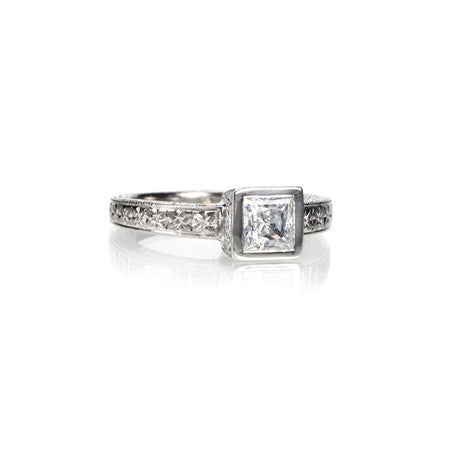 Crafted in 14KT white gold this ring features a bezel set princess-cut on an orange blossom hand-engraved band.