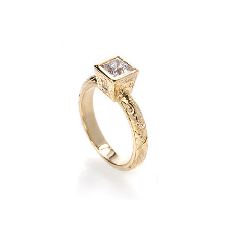 Crafted in 14KT yellow gold, this ring features a bezel set princess-cut diamond with accent diamonds on either side on a paisley hand-engraved band.