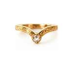 A yellow gold v-shank ring with an ornate filigree pattern and a central round-cut clear gemstone, shown on a plain white background.