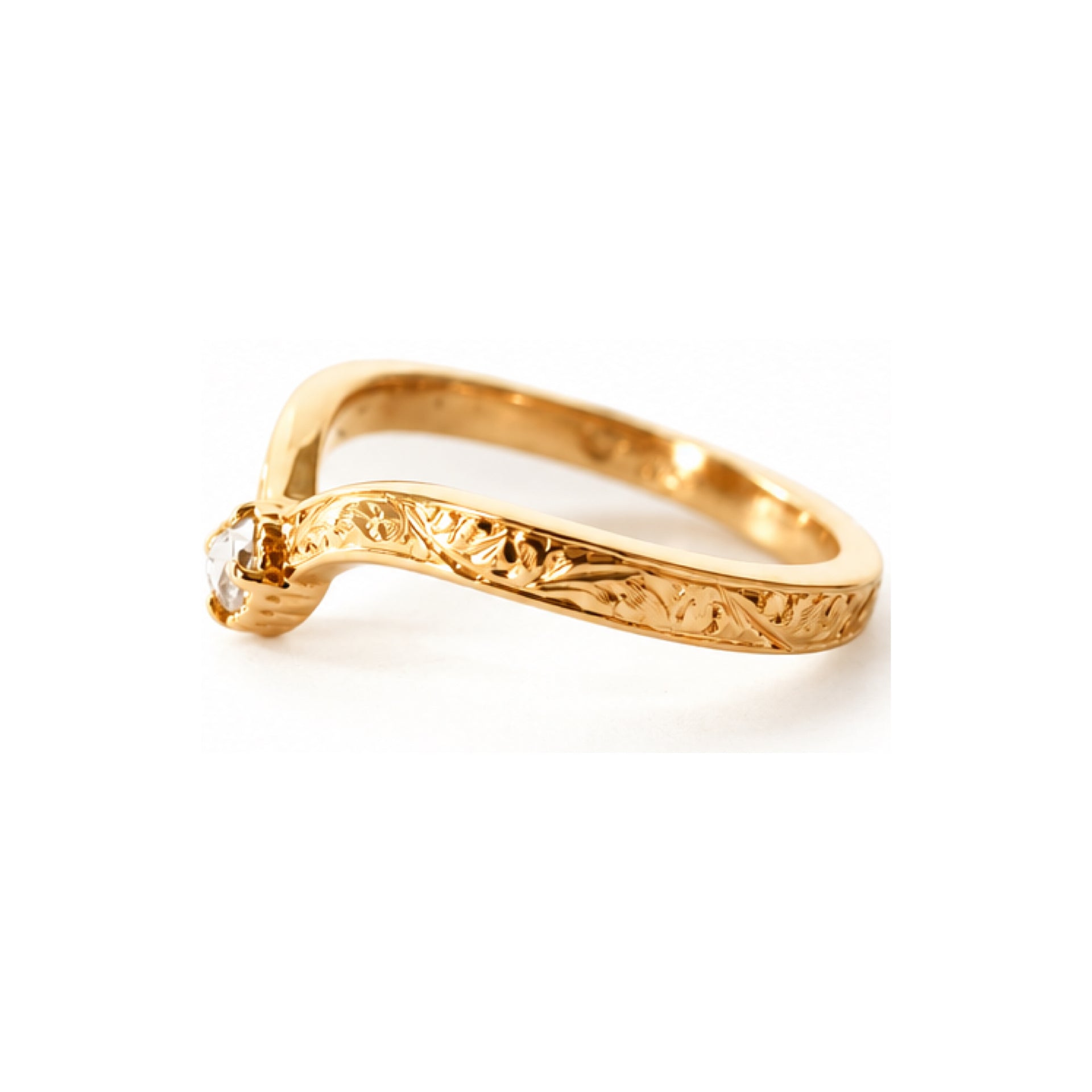 A gold ring with an ornate, engraved band and a single clear gemstone in a prong setting, shown on a plain white background.