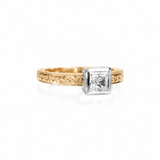 Crafted in 14KT gold, this engagement ring features a princess cut diamond set in a 14KT gold square bezel setting on an orange blossom hand engraved band. 