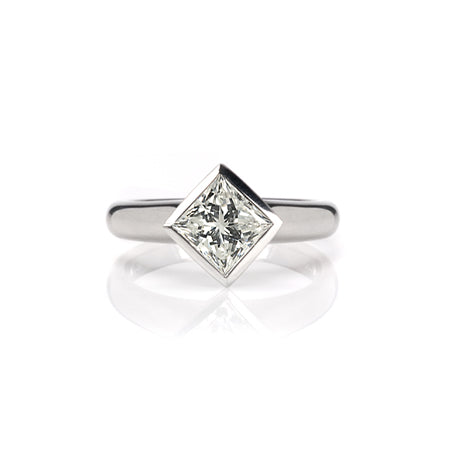 Crafted in 14KT gold, this engagement ring features a bezel set princess-cut diamond. 