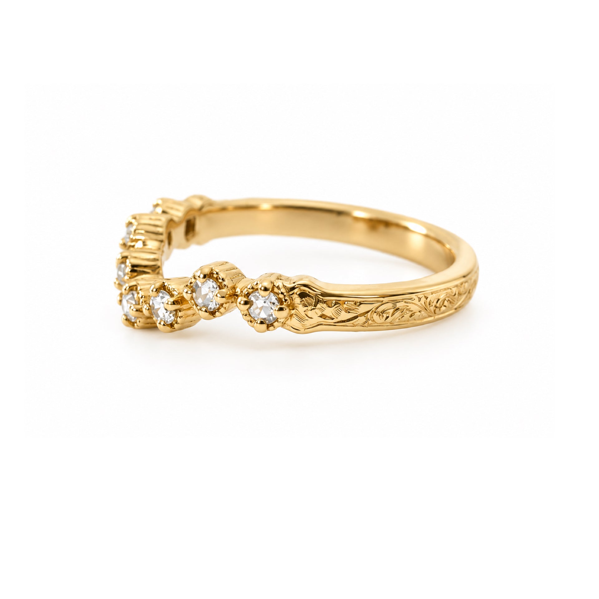 A yellow gold ring featuring a row of small round-cut clear gemstones and an engraved floral pattern on the band, shown against a plain white background.