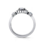 A silver-toned diamond ring with a central round-cut diamond and smaller diamonds set in decorative side clusters, shown from the back on a white background.