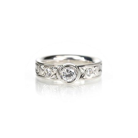 Crafted in 14KT gold, this comfort-fit engagement ring is set with a round brilliant-cut diamond between two smaller round brilliant-cut diamonds on a paisley hand-engraved band. 