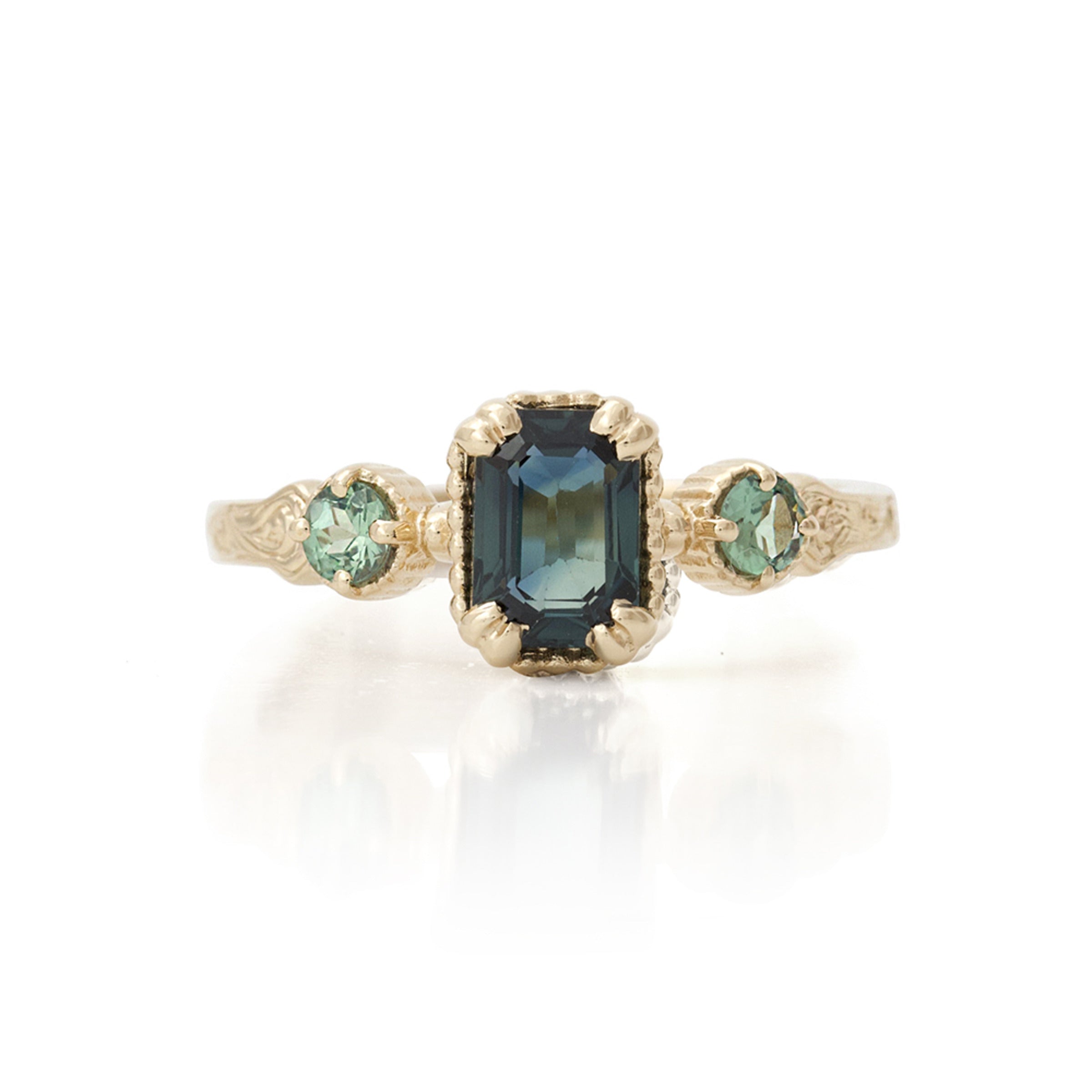 A vintage-style ring featuring a large emerald cut sapphire centerpiece with two round alexandrite accents, set in hand-engraved 14KT yellow gold.