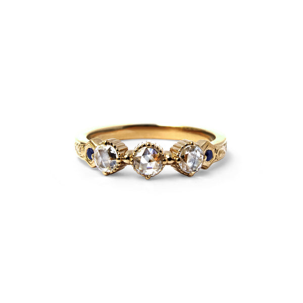 Crafted in 14KT yellow gold, this ring features 3 round brilliant-cut diamonds in a row, with a blue sapphire on either side on a vintage-inspired hand engraved band.