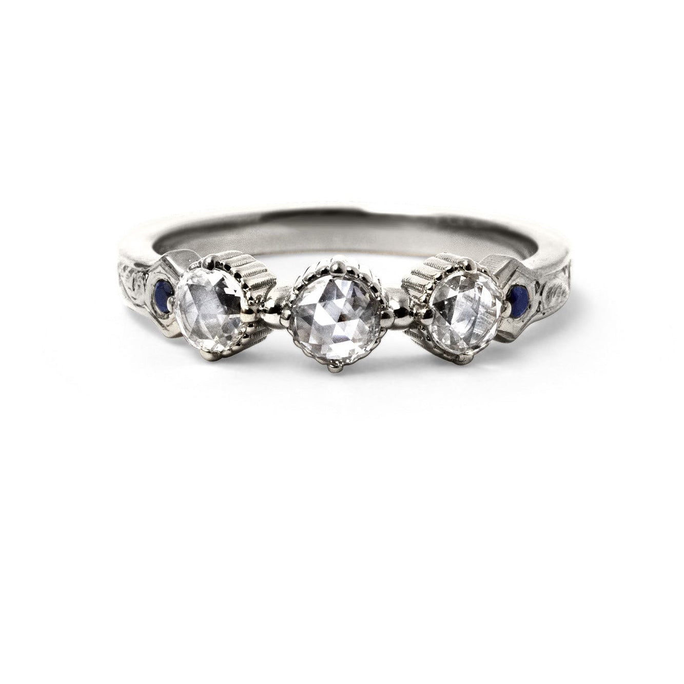 Crafted in 14KT white gold, this ring features 3 round brilliant-cut diamonds in a row, with a blue sapphire on either side on a vintage-inspired hand engraved band.