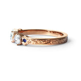 Crafted in 14KT yellow gold, this ring features 3 round brilliant-cut diamonds in a row, with a blue sapphire on either side on a vintage-inspired hand engraved band.