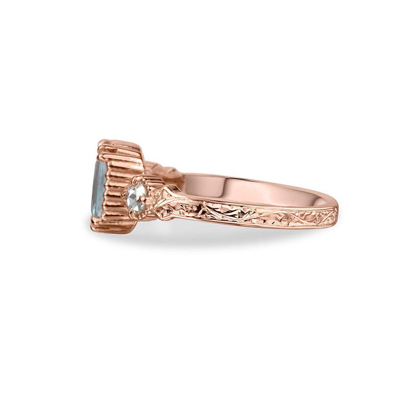 Crafted in 14KT rose gold, this ring features an aquamarine between two round brilliant-cut diamonds on a vintage-inspired hand engraved band.
