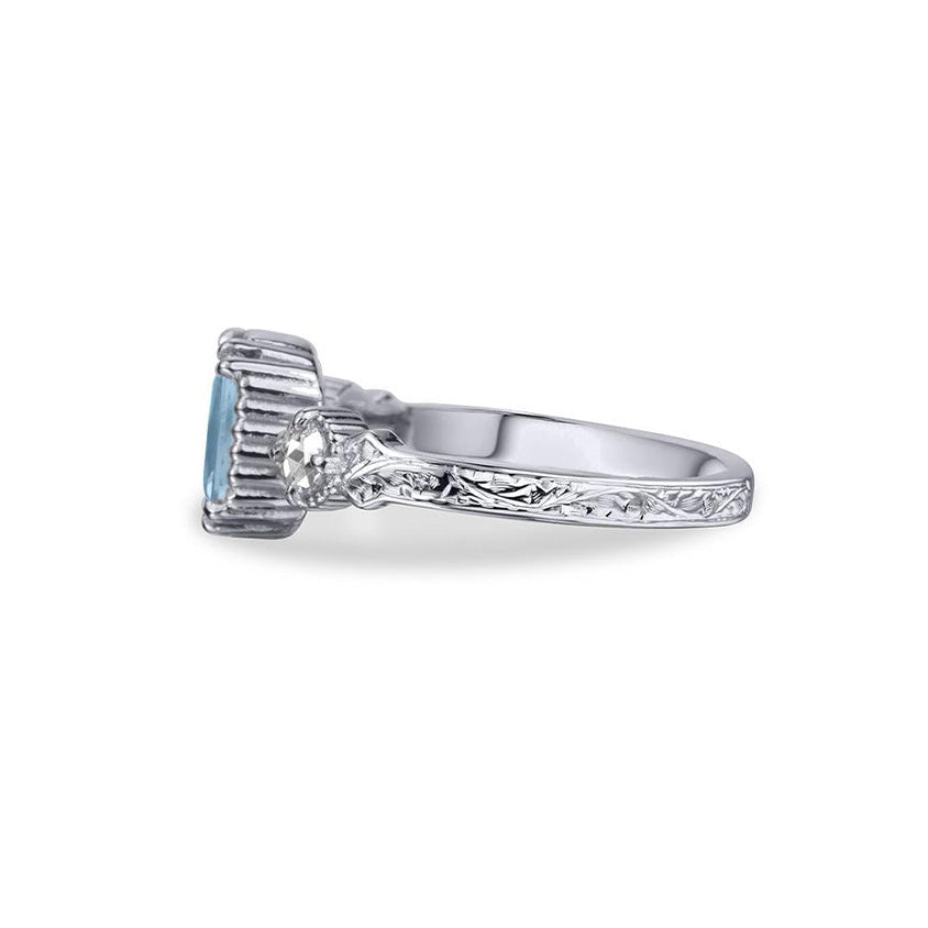 Crafted in 14KT white gold, this ring features an aquamarine between two round brilliant-cut diamonds on a vintage-inspired hand engraved band.