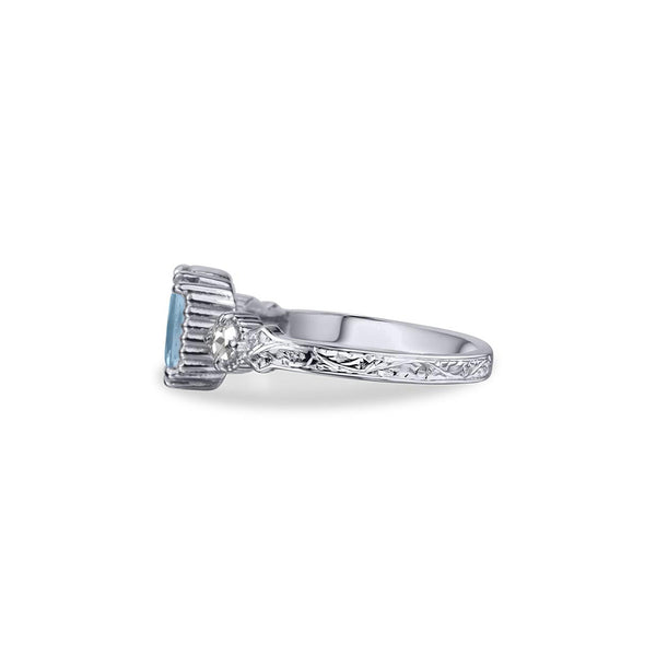 Crafted in 14KT white gold, this ring features an aquamarine between two round brilliant-cut diamonds on a vintage-inspired hand engraved band.