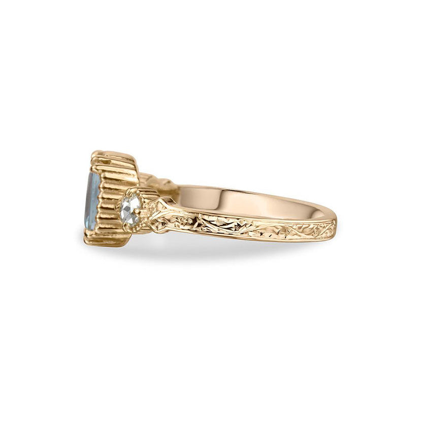 Crafted in 14KT yellow gold, this ring features an aquamarine between two round brilliant-cut diamonds on a vintage-inspired hand engraved band.