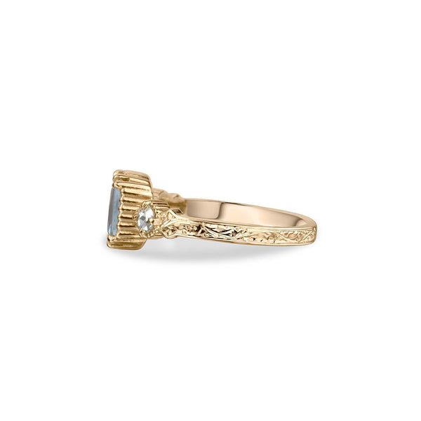 Crafted in 14KT yellow gold, this ring features an aquamarine between two round brilliant-cut diamonds on a vintage-inspired hand engraved band.