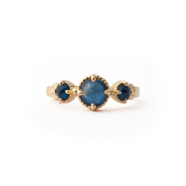 Crafted in 14KT yellow gold, this ring features a blue sapphire set between two smaller ones on a vintage-inspired hand engraved band. 