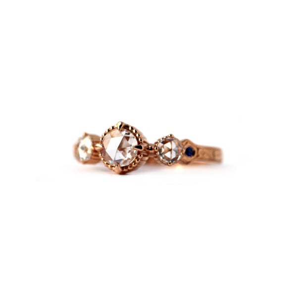 Crafted in 14KT rose gold, this ring features a large rose-cut diamond with a smaller diamond and a blue sapphire on each side. All on a vintage-inspired hand engraved band.