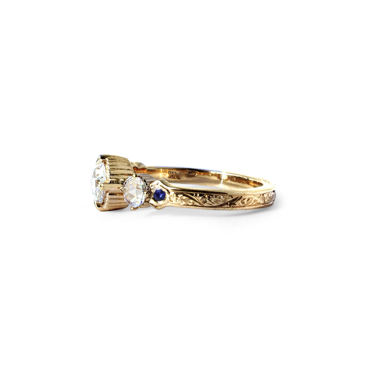 Crafted in 14KT yellow gold, this ring features a large rose-cut diamond with a smaller diamond and a blue sapphire on each side. All on a vintage-inspired hand engraved band.